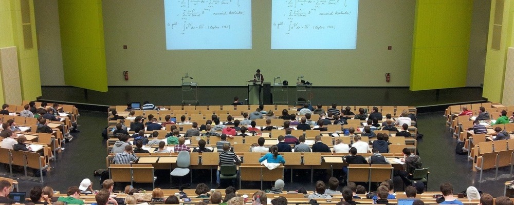 Lecture hall with students sitting at desks and  professor teaching