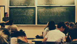 Students sitting at desks with a techer writting on chalkboard