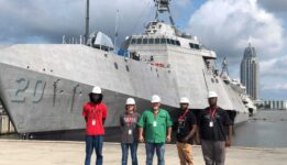 Welding students standing in front of a battleship at Austal